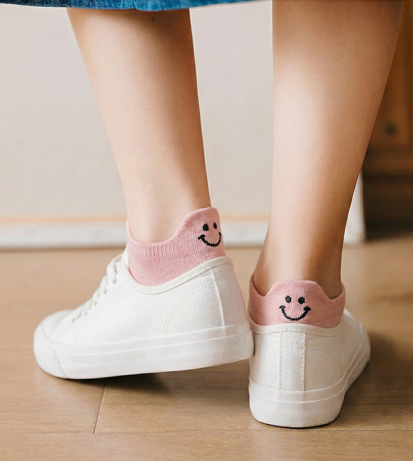 Pink socks with smiley faces worn with white sneakers on a wooden floor.